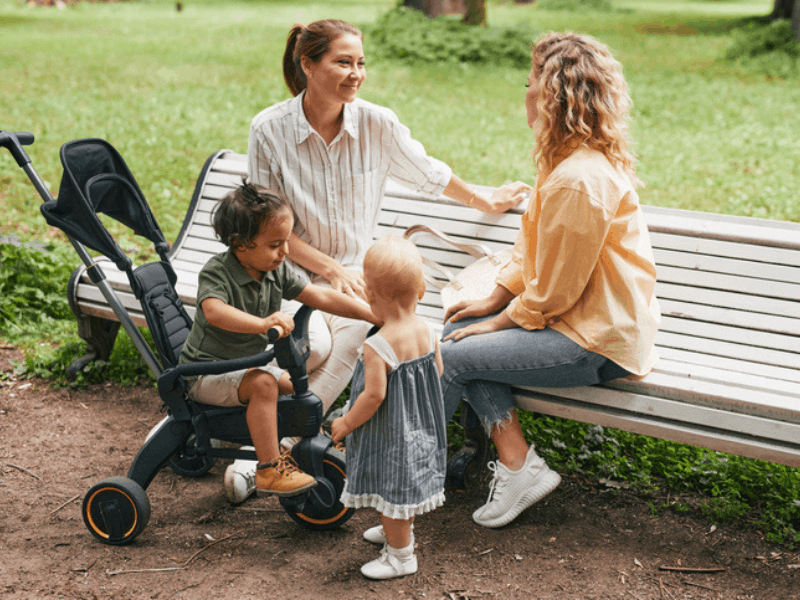 Two moms sitting on a park bench with their children