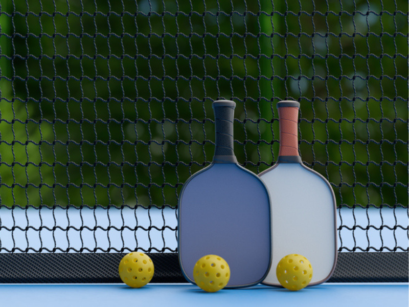 Two pickleball paddles and balls on a court leaning on a net