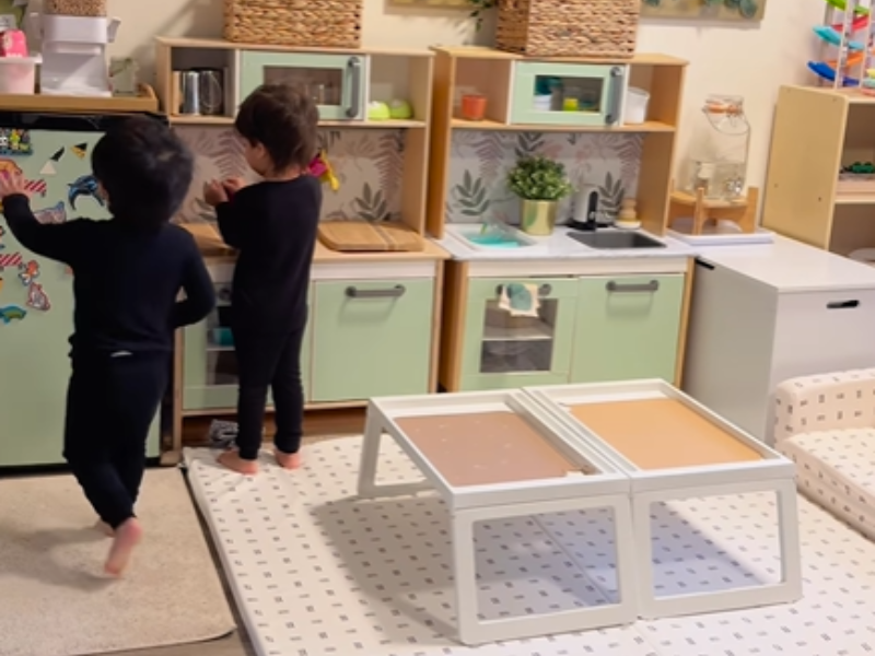Two toddlers walking around their mini kitchen