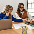 Two young women using their laptops in a corporate setting