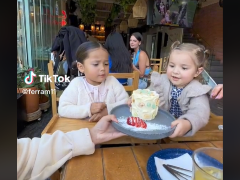 Two young girls look at a mini cake that is handed to them