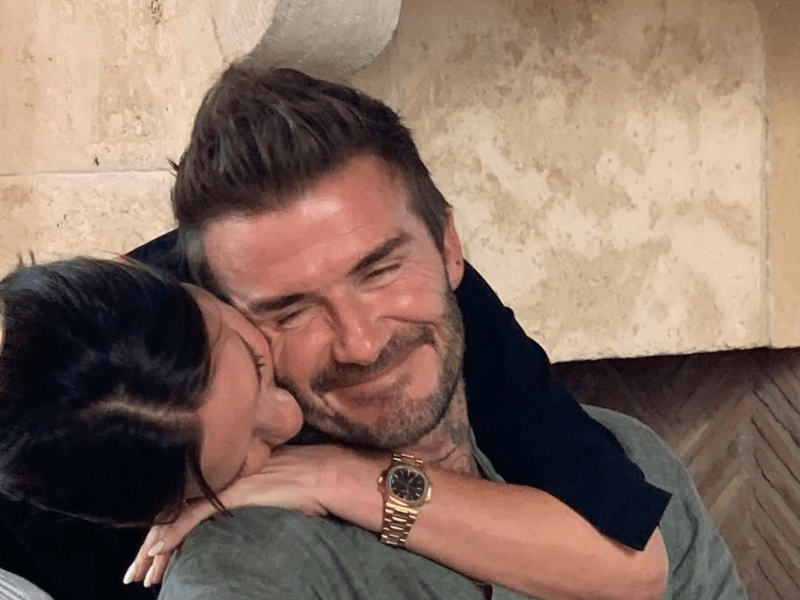 David Beckham smiles as wife Victoria Beckham hugs him