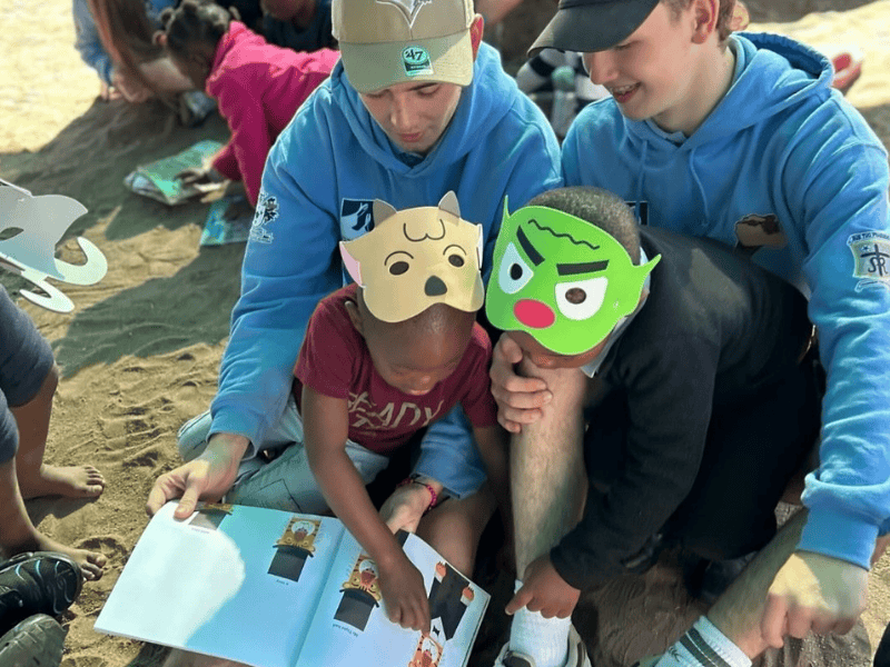 Volunteers sit on the ground with school children reading books