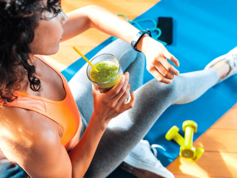 Woman wearing fitness attire drinks green smoothie
