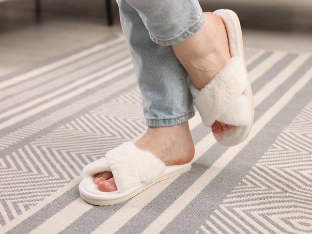 Woman in stylish slippers on rug at home
