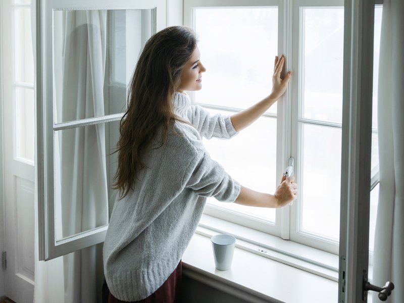 Woman in warm woolen pullover is opening window