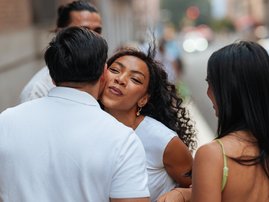 Woman kissing man on cheek greeting friends on city street