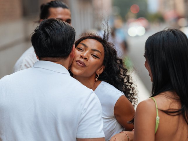 Woman kissing man on cheek greeting friends on city street