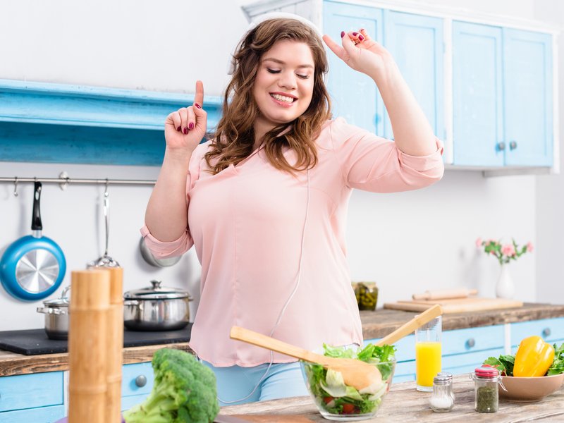 Woman listening music at table with fresh vegetables in kitchen iStock
