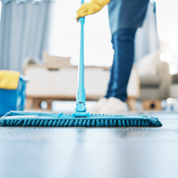 Woman wearing yellow gloves mops the floor with a blue mop