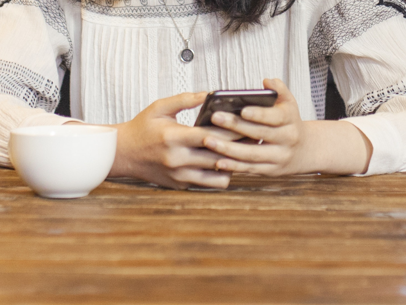 Woman seated at a table with her phone and a cup of coffee