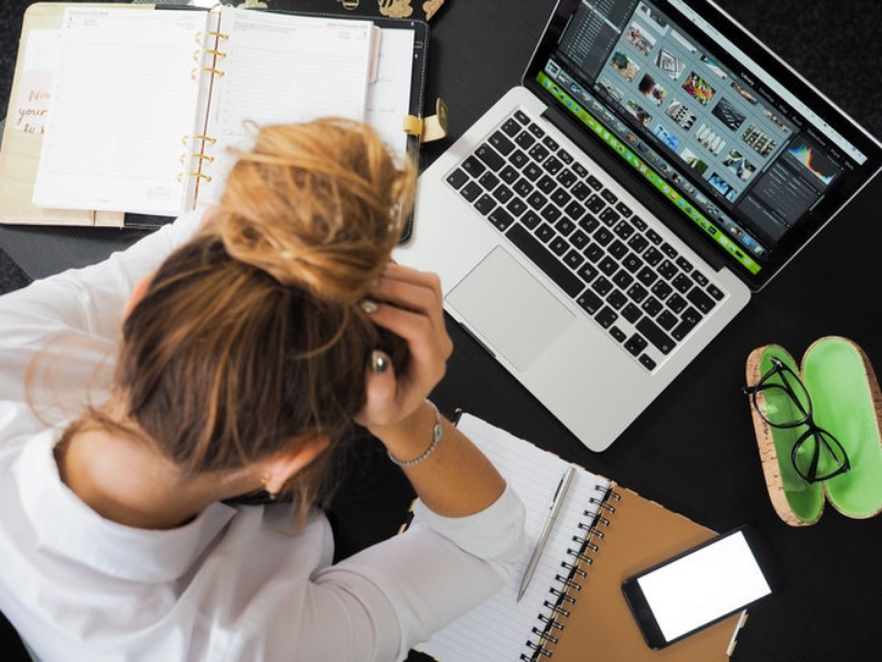 Woman sitting in front of her laptop holding her head in her hands
