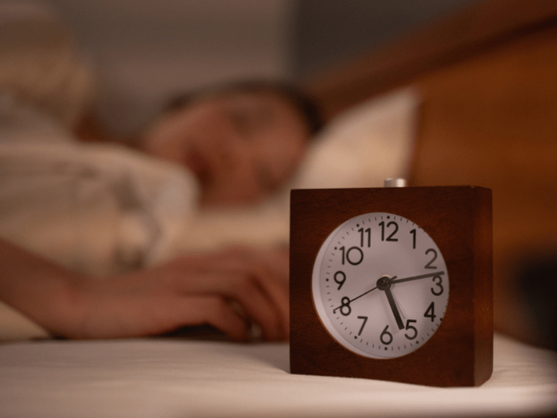Woman sleeping on bed next to alarm clock