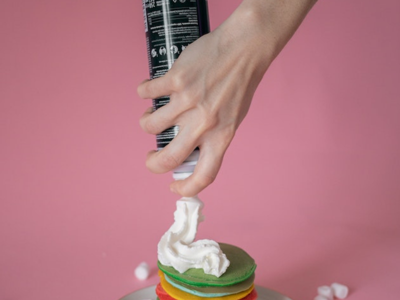 Woman spraying whipped cream on colourful pancakes