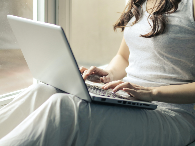 Woman wearing a tank top sitting by the window with her laptop