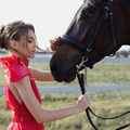 Woman wearing fancy red dresses poses next to a horse