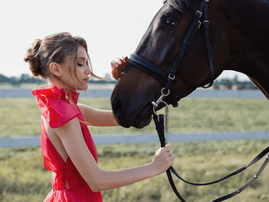 Woman wearing fancy red dresses poses next to a horse