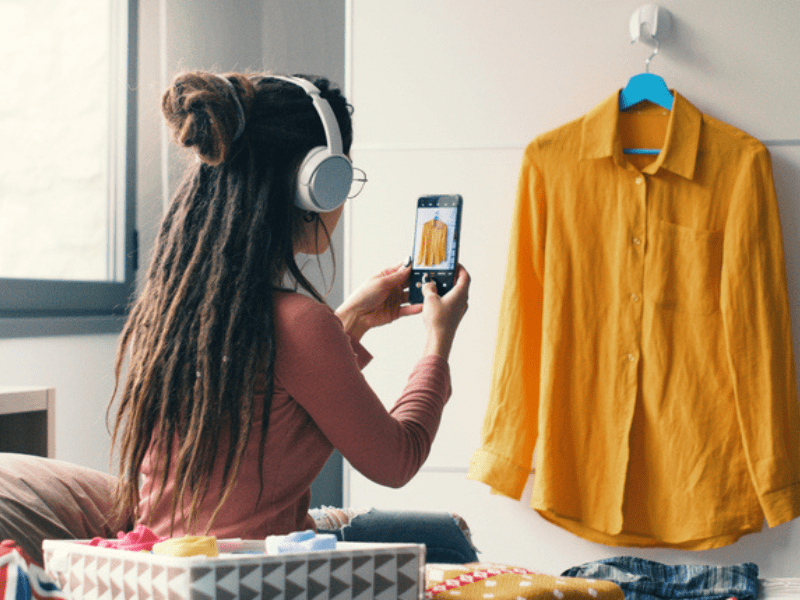 Woman wearing headphones takes pictures of her clothes in a bedroom