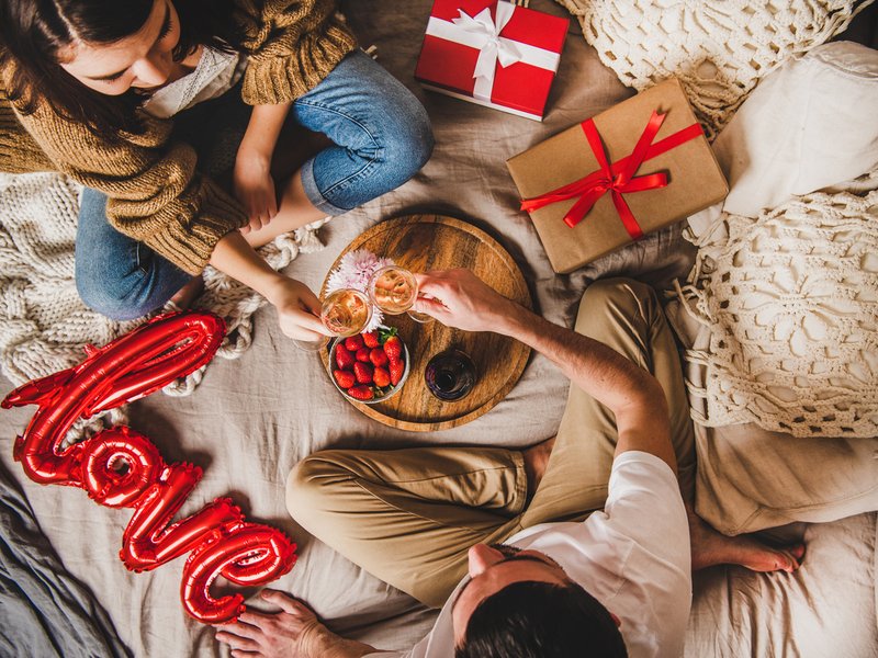 Young couple sitting in bed, giving presents drinking rose champagne