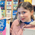 Young girl wearing pink jacket holds up two books by Roald Dahl