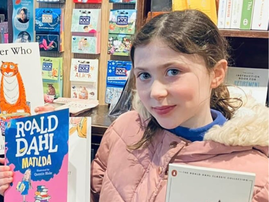 Young girl wearing pink jacket holds up two books by Roald Dahl