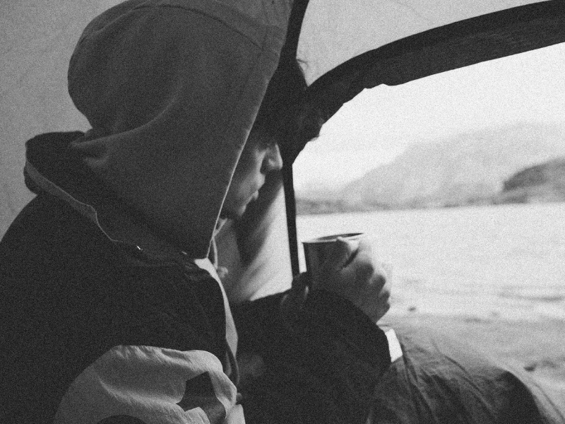 Young man drinking hot beverage from inside his tent