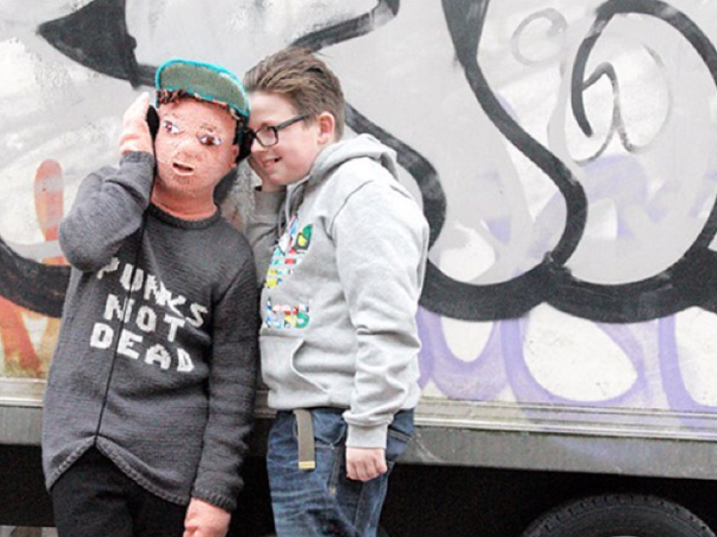 Young man standing next to a life size knitted doll