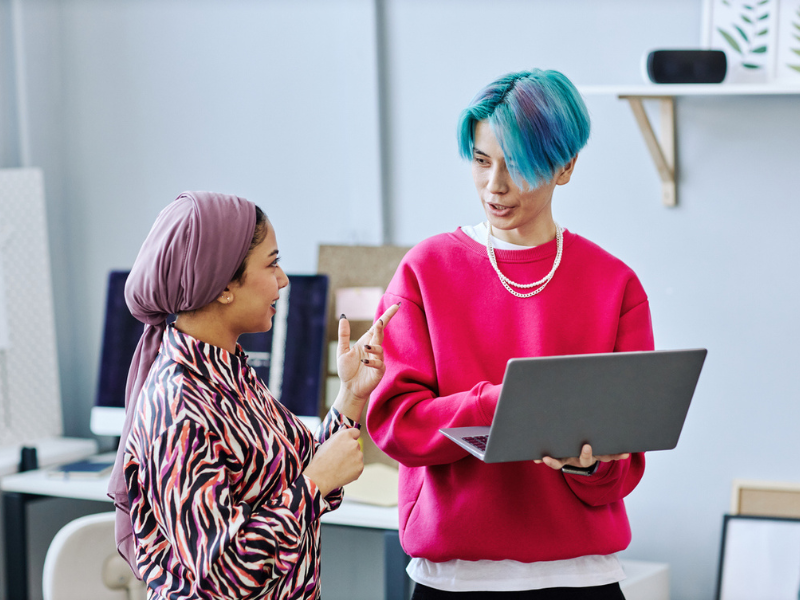 Young man with blue and purple hair carrying a laptop