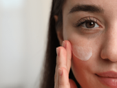 Young woman with dry skin applying cream onto her face
