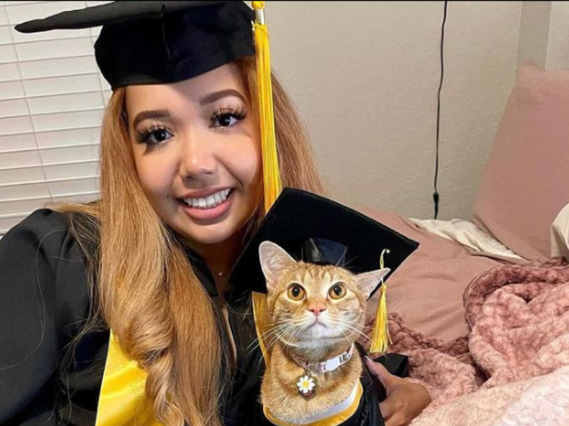 Young woman with graduation gown and cat dressed in graduation outfit