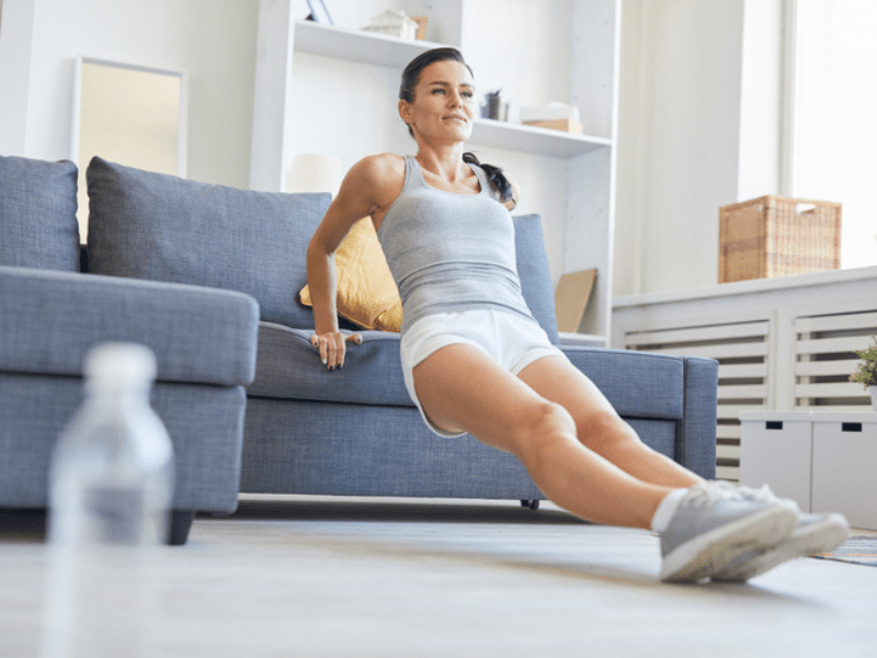 Brunette woman exercising by a sofa in living-room