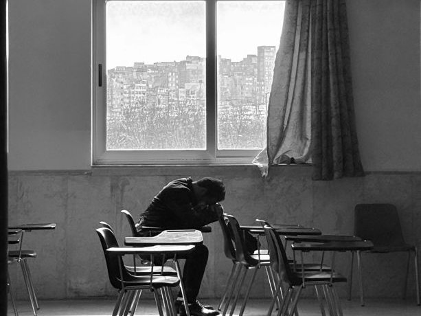 A student with his head down on a school desk in empty classroom