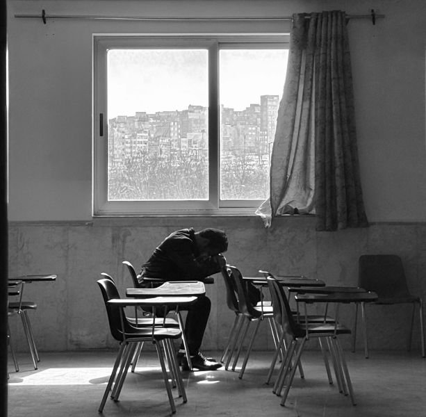 A student with his head down on a school desk in empty classroom