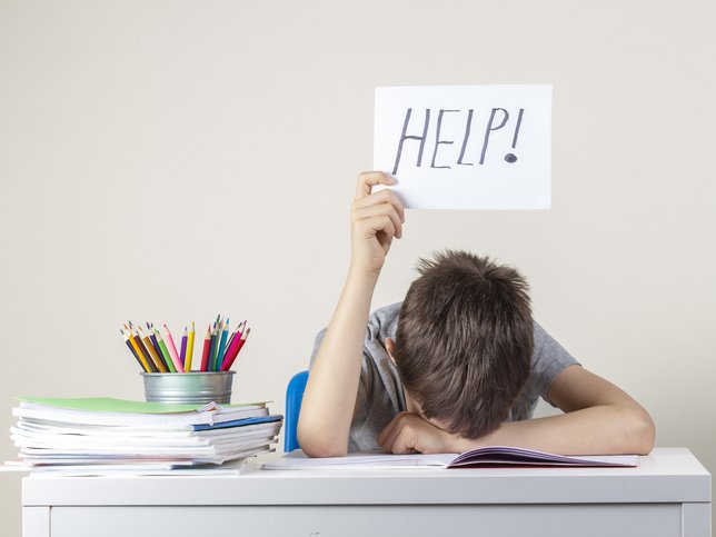 A boy sitting at the table with many books and holding paper with word Help