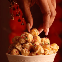 Hand reaching for burfee popcorn in a glass bowl