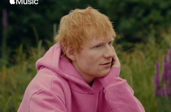 Ed sheeran wearing a pink hoodie with a Play icon