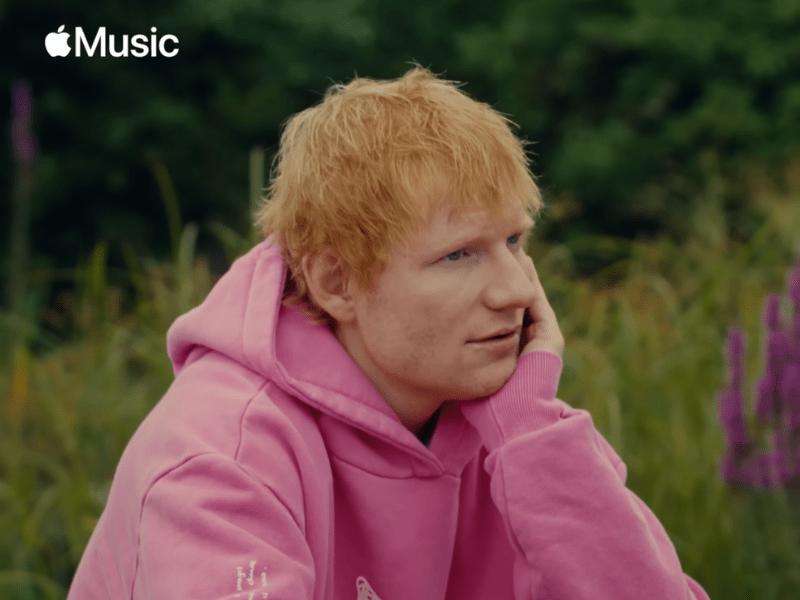 Ed sheeran wearing a pink hoodie with a Play icon