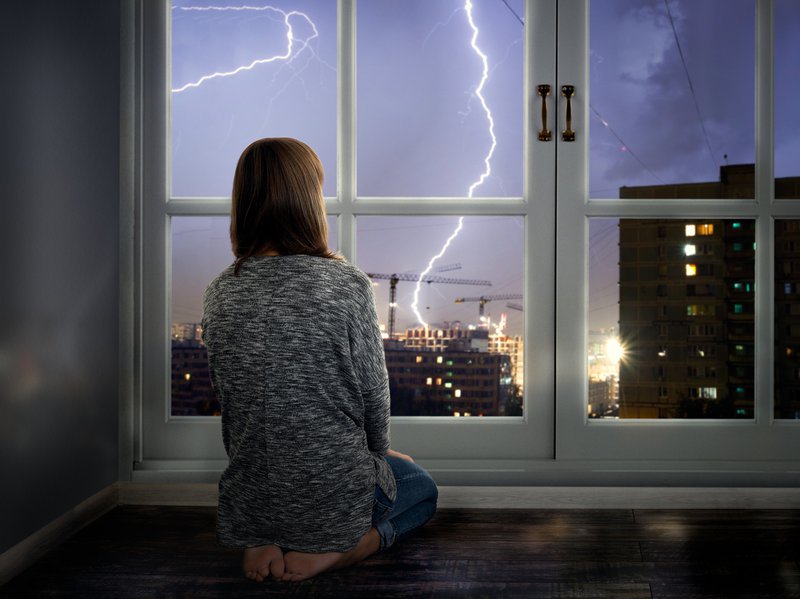 Girl looking through window during thunderstorm