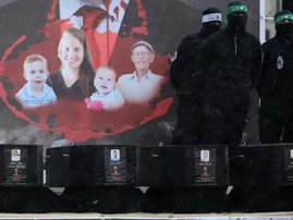 Palestinian militant group Hamas fighters stand on stage next to the coffins of the four Israeli hostages during the handing them over to the Red Cross in Khan Yunis in the southern Gaza