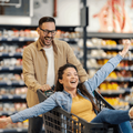 happy man pushes woman in a grocery store trolley