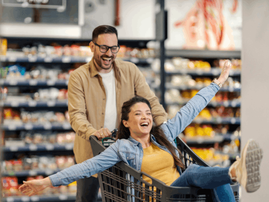 happy man pushes woman in a grocery store trolley