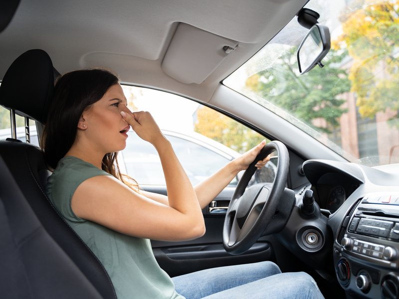 A woman blocking her nose to prevent bad odour from car