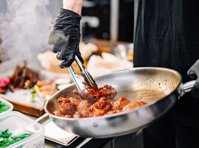 Woman chef cooking chicken wings in a sauce in the kitchen stock photo