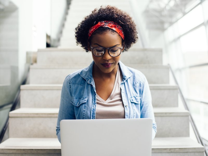 Focused young woman sitting on stairs using a laptop / iStock