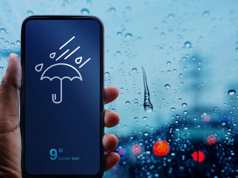 Rainy Day Concept. Hand Holding Smartphone with Weather Information show on Screen.