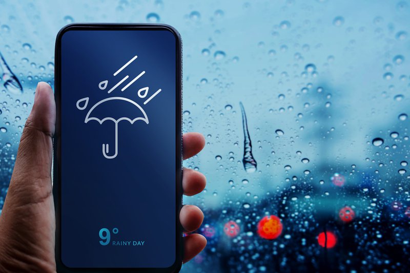 Rainy Day Concept. Hand Holding Smartphone with Weather Information show on Screen.