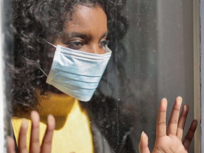 A woman wearing a mask standing by window