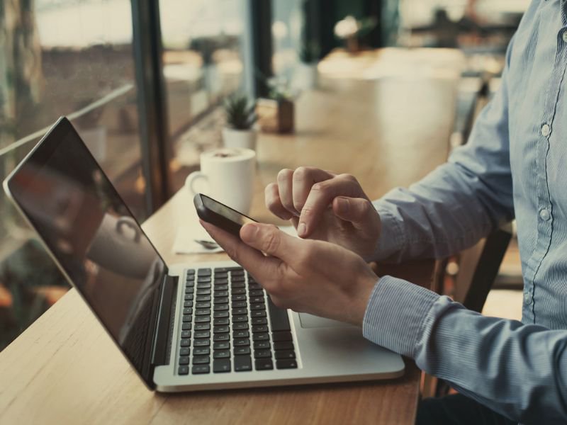 man in shirt using smartphone and laptop