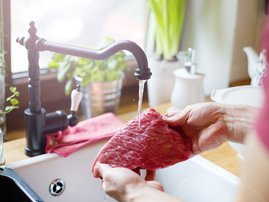 A person in the kitchen rinsing beef steak