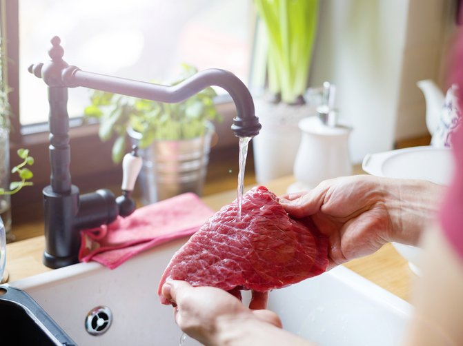 A person in the kitchen rinsing beef steak